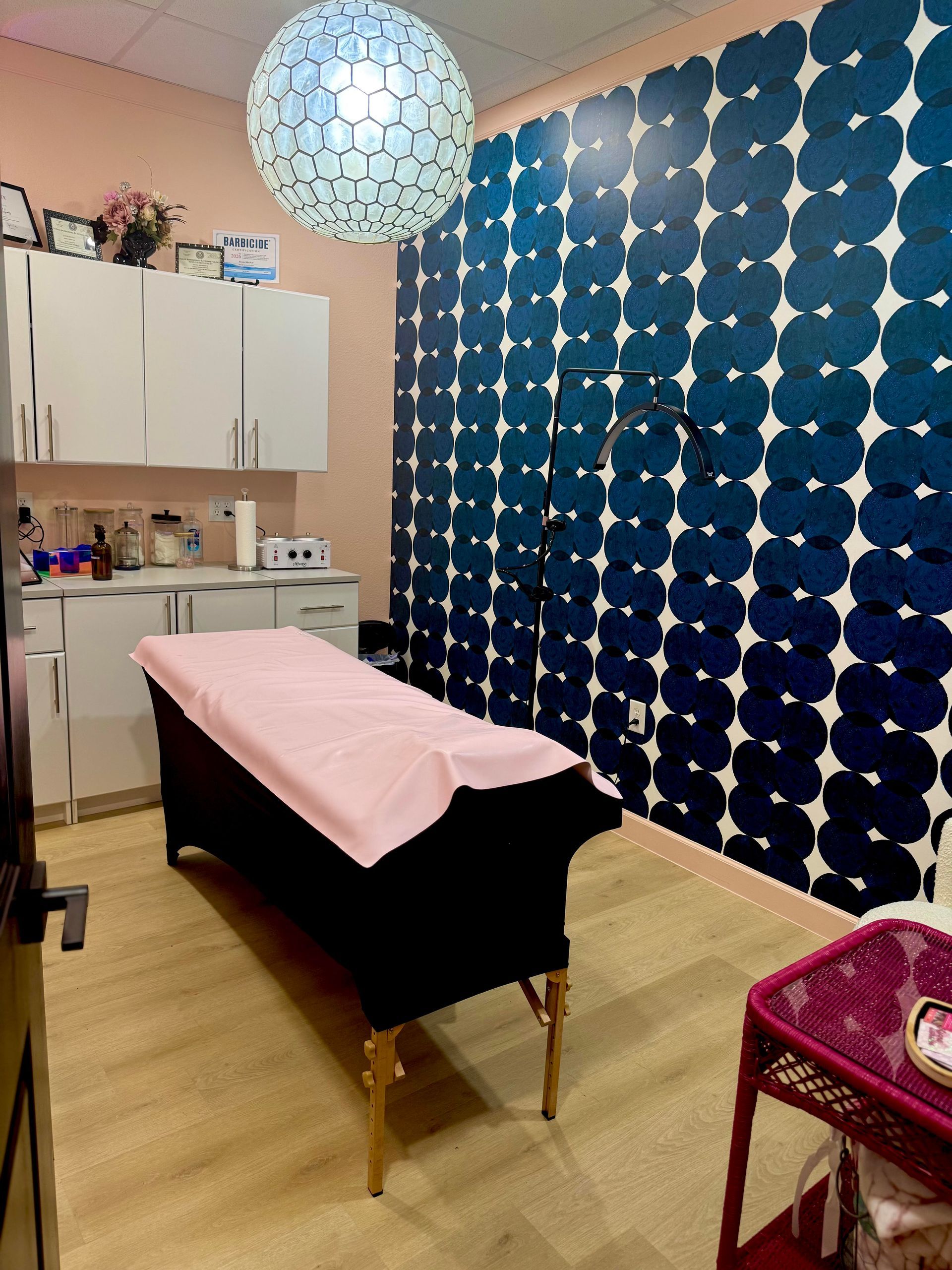 Treatment room with massage table, pink cover, blue patterned wall, and white cabinets