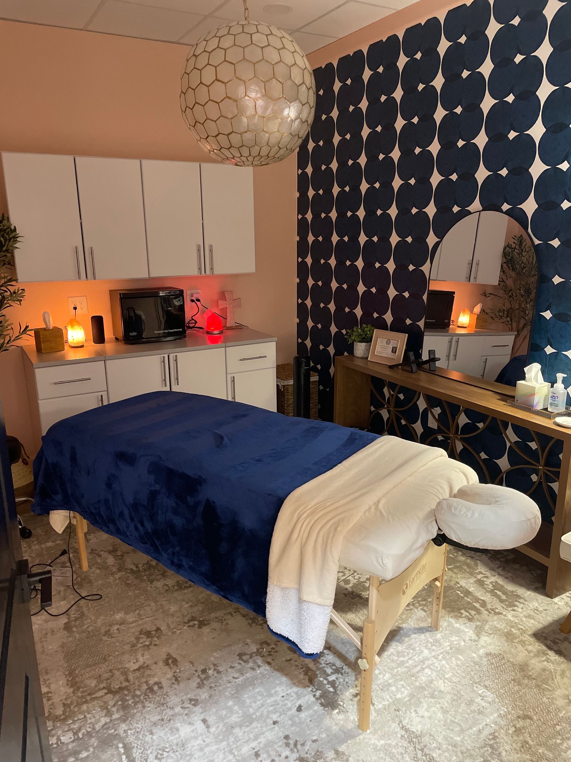 Cozy bedroom with a blue bedspread, white desk cabinets, patterned navy wall, and warm ambient lighting